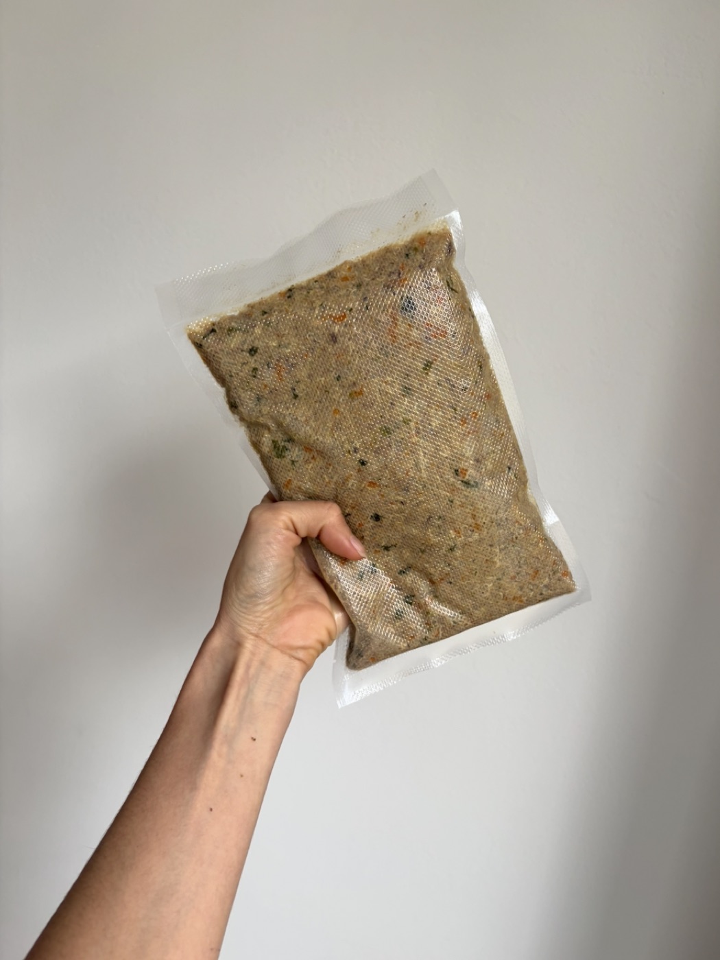 Una mano sostiene una bolsa al vacío de la Receta de la casa: se ven la carne, la zanahoria y la espinaca